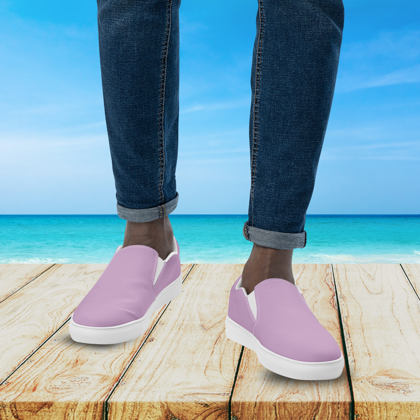 Person wearing purple slip-on shoes with blue jeans standing on a wooden platform by the ocean.
