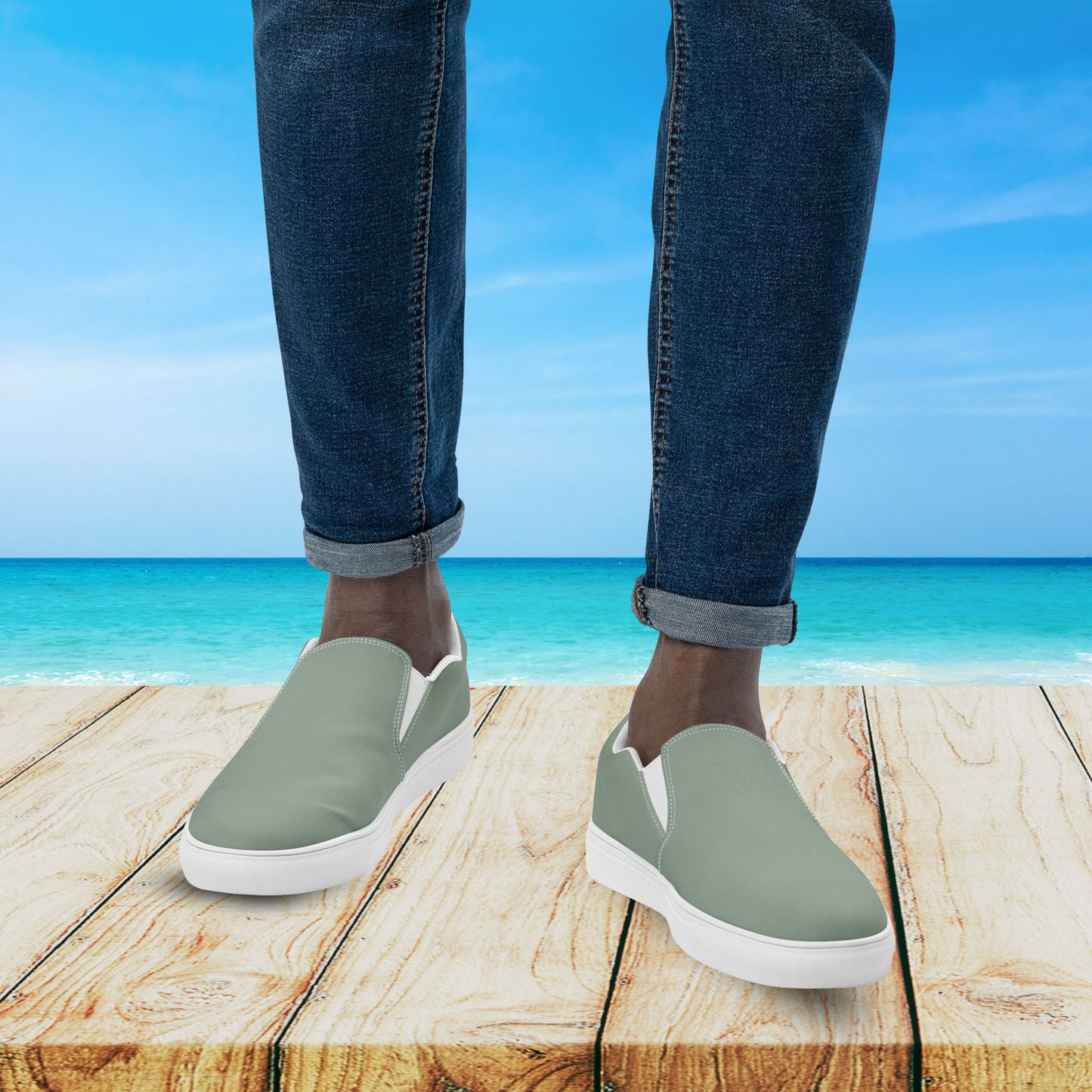 Person wearing green slip-on shoes with white soles on a wooden platform by the ocean.