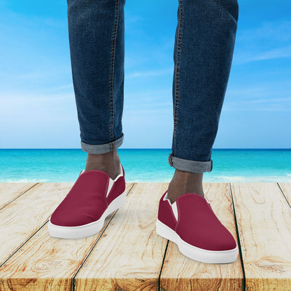 Red slip-on shoes with white soles worn by a person standing on a wooden platform with a beach background.