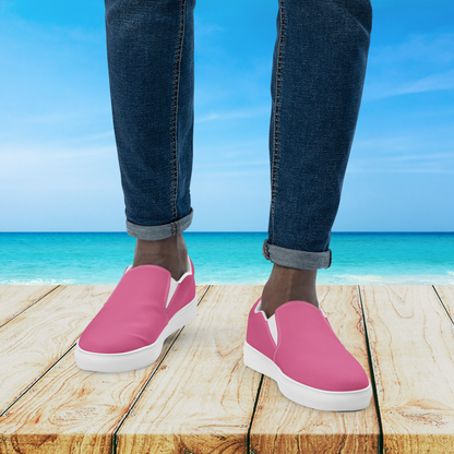 Person wearing pink slip-on shoes with blue jeans standing on a wooden platform by the ocean.