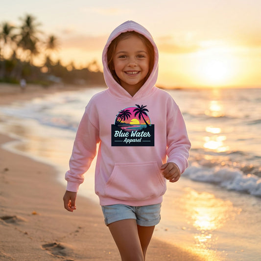 child model wearing light pink neon sunset kids hoodie running down beach by blue water apparel