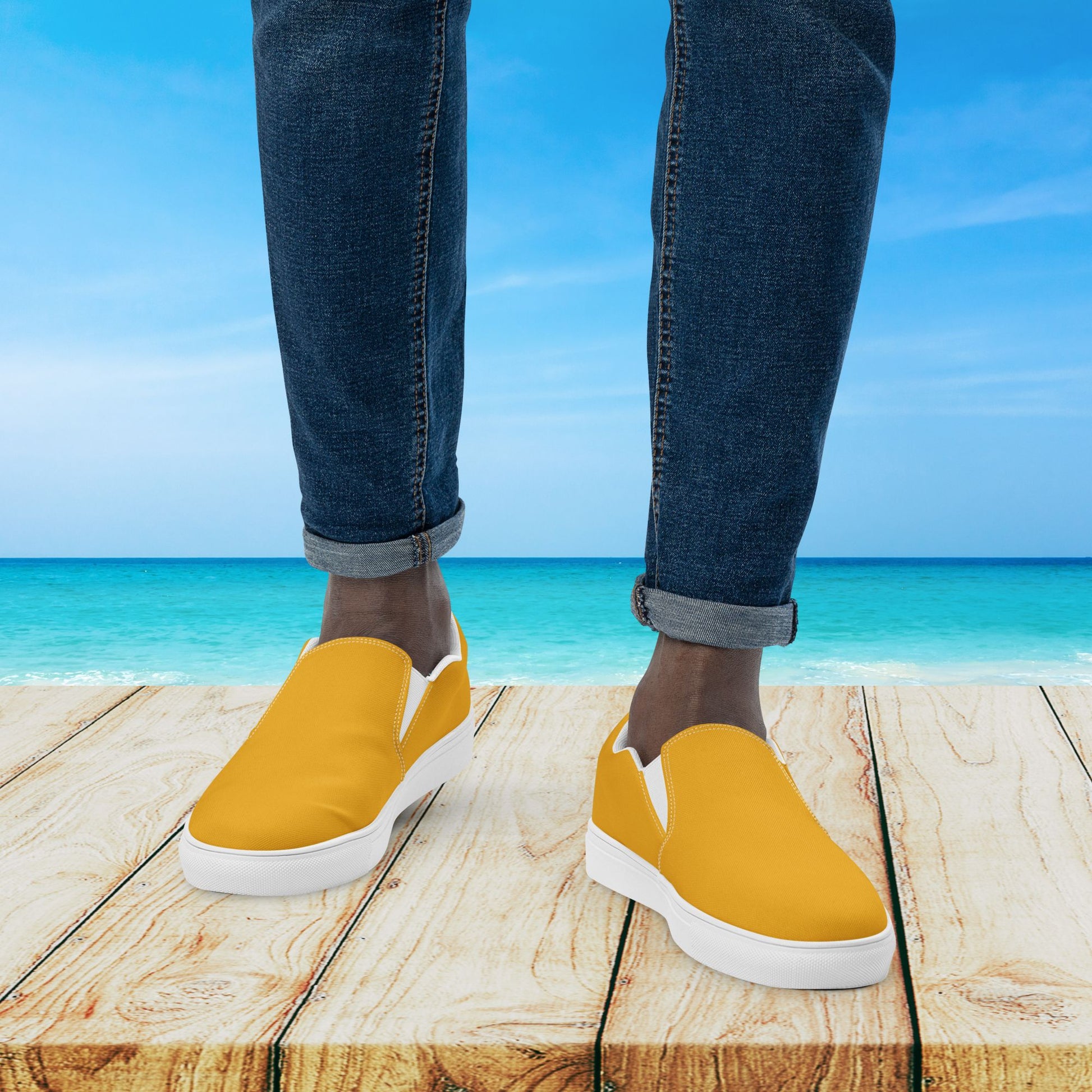 Yellow slip-on shoes with white soles worn by a person standing on a wooden platform with a beach background.