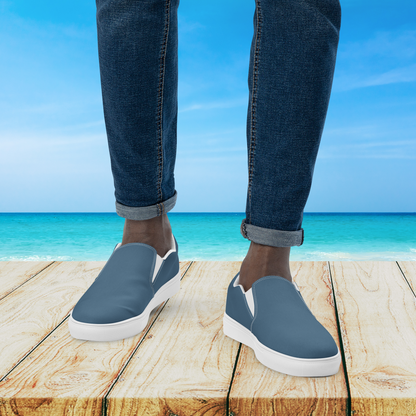 Person wearing blue slip-on shoes with white soles on a wooden platform by the ocean.