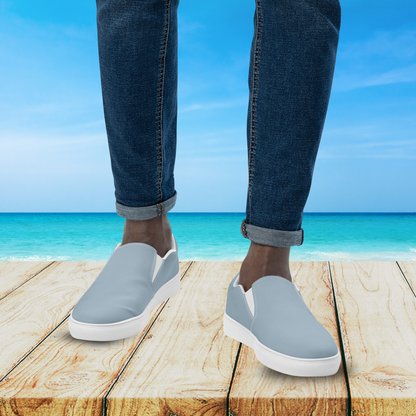 Person wearing light gray slip-on shoes with white soles on a wooden platform by the ocean.