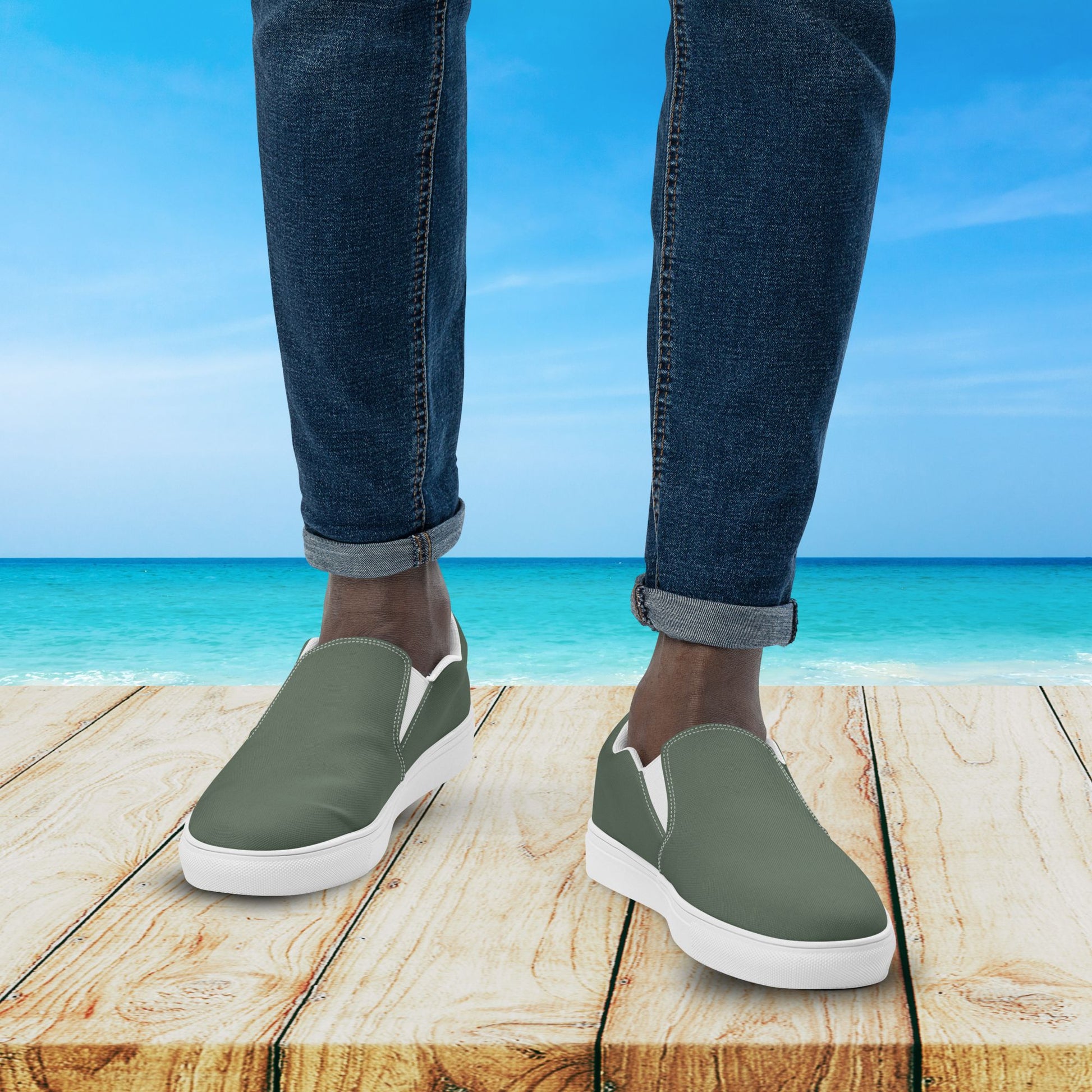Person wearing green slip-on shoes with white soles on a wooden platform by the ocean.
