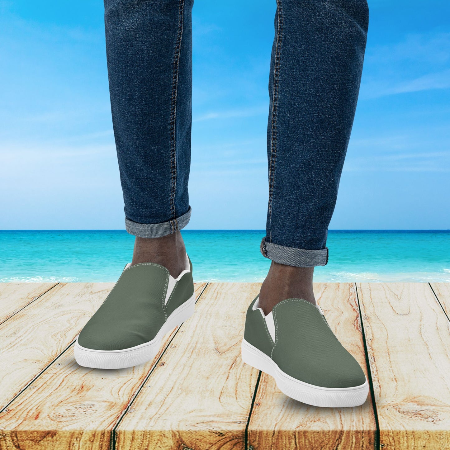 Person wearing green slip-on shoes with white soles on a wooden platform by the ocean.