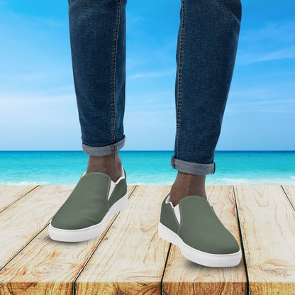 Person wearing green slip-on shoes with white soles on a wooden platform by the ocean.