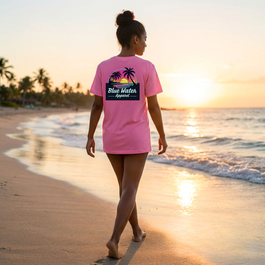 woman wearing charity pink neon sunset adult tee walking down beach by blue water apparel