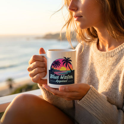 woman holding the neon sunset coffee mug sitting on deck overlooking beach by blue water apparel