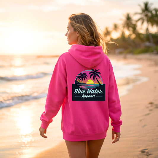 female model on beach wearing heliconia neon sunset adult hoodie on beach by blue water apparel