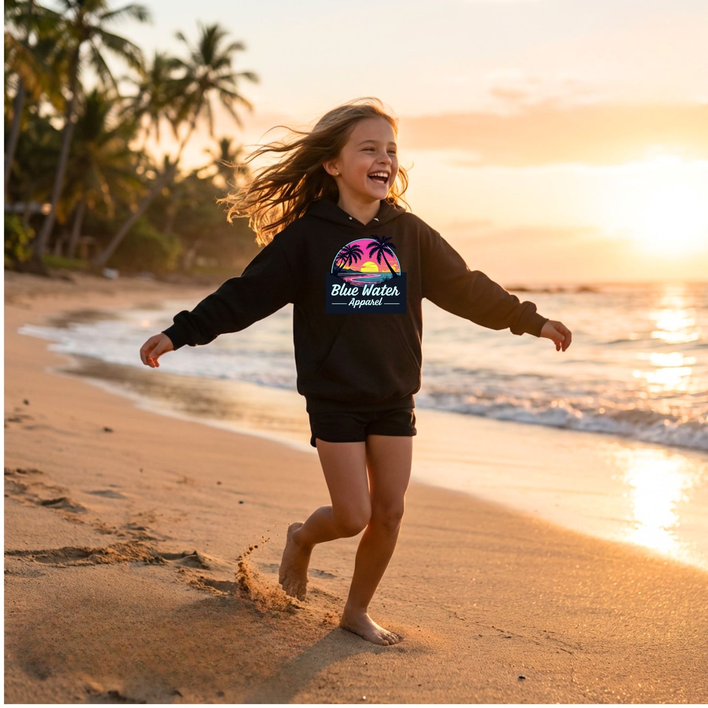 child model wearing black neon sunset kids hoodie running down beach by blue water apparel