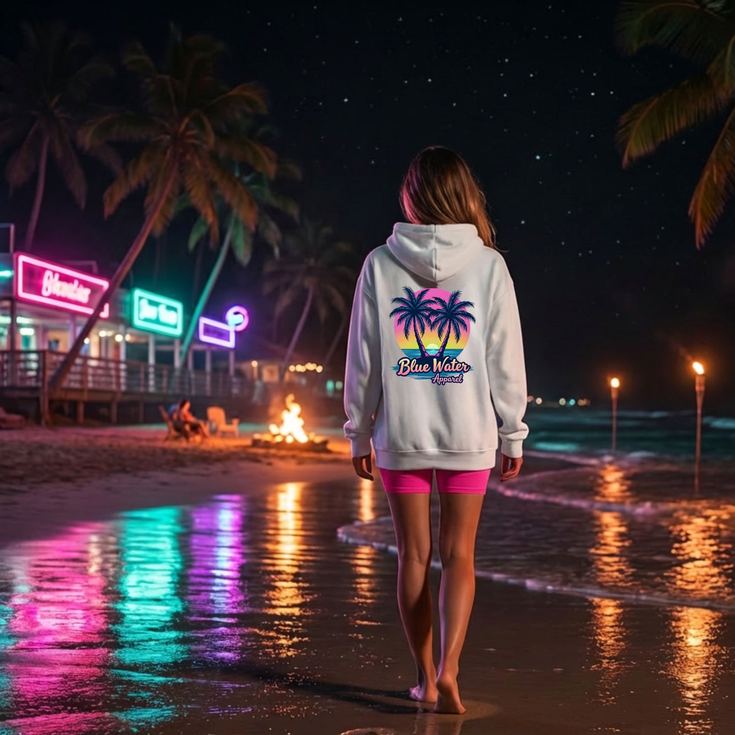 woman wearing white neon tropics hoodie walking down neon lit beach by blue water apparel