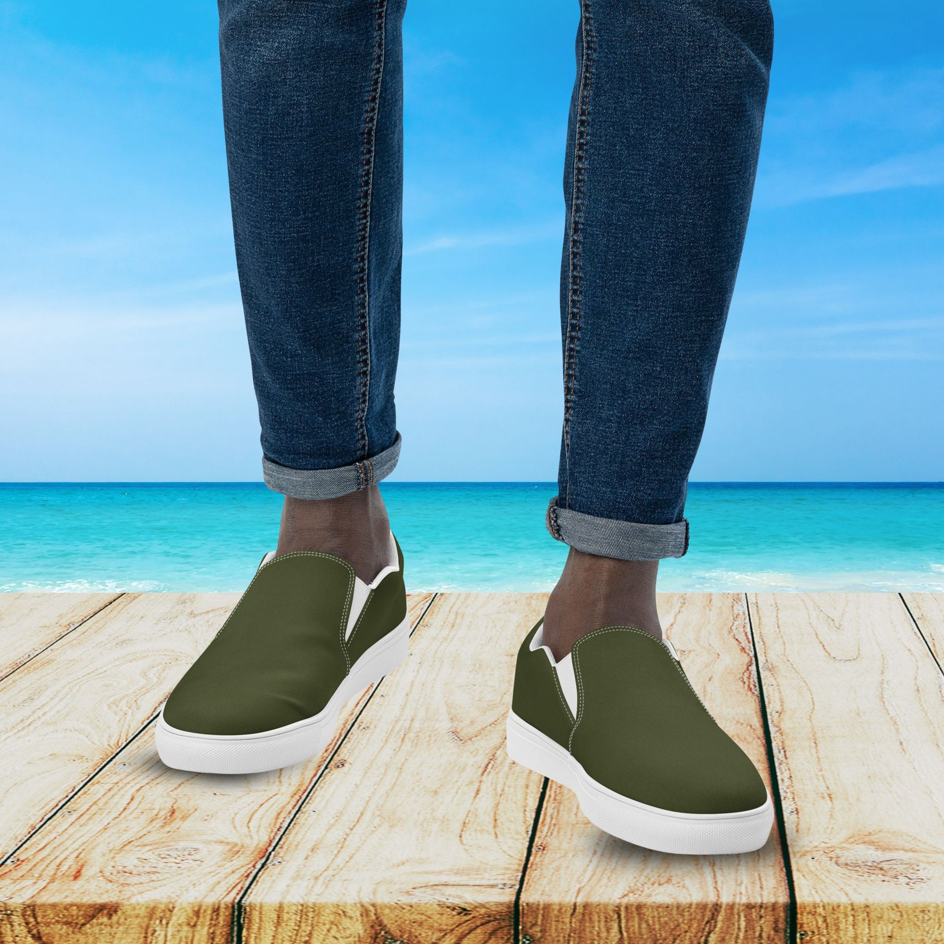 Person wearing green slip-on shoes with white soles on a wooden platform by the ocean.