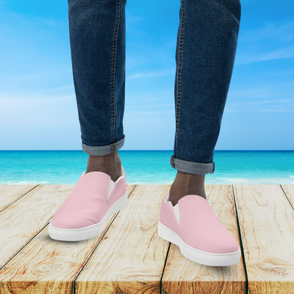 Person wearing pink slip-on shoes with blue jeans standing on a wooden platform by the ocean.