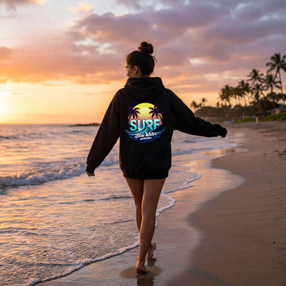 female model wearing black retro surf adult hoodie on beach by blue water apparel