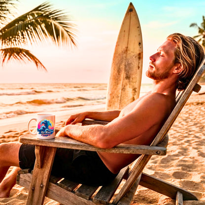man sitting in chair on the beach with surfboard in background with the retro wave coffee mug by blue water apparel.