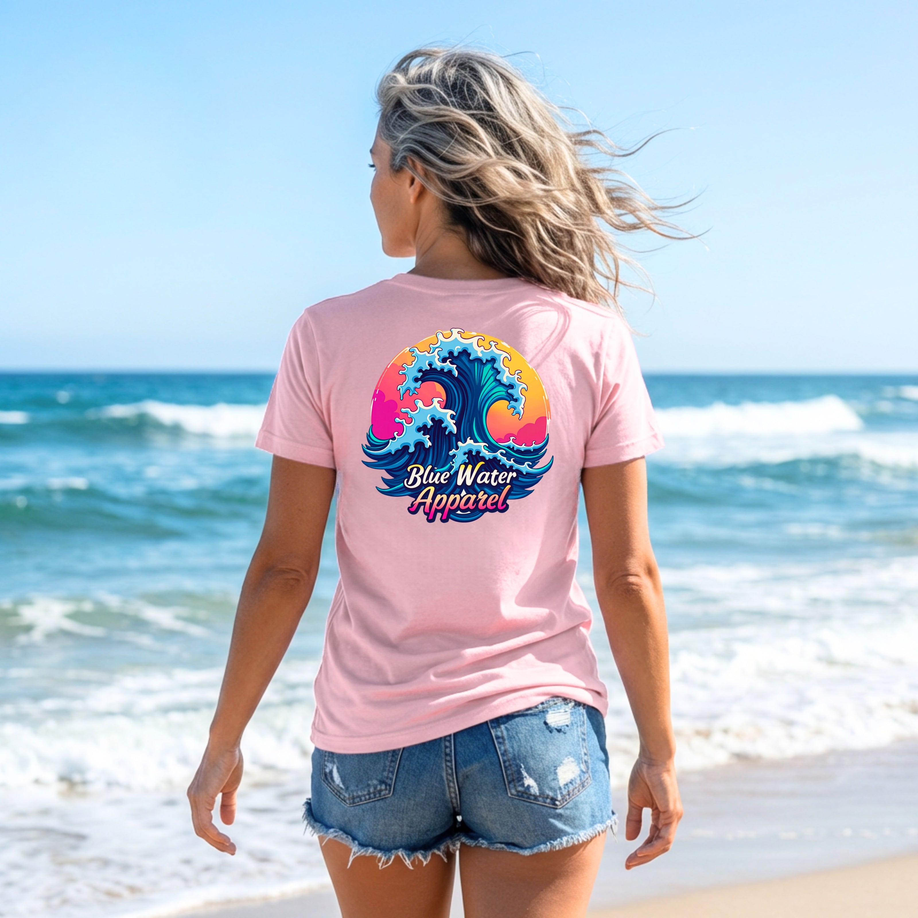 woman wearing pink retro wave adult tee standing on beach by blue water apparel