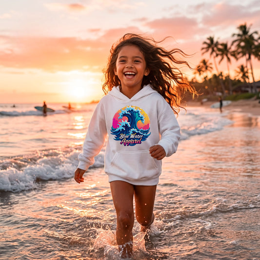 girl wearing white retro wave kids hoodie running through water on beach by blue water apparel