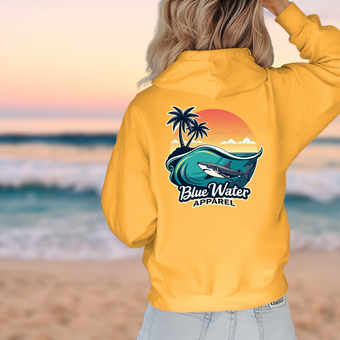 woman on beach wearing gold shark wave hoodie by blue water apparel