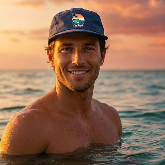 man wearing petrol blue shark wave surf cap sitting in ocean water by blue water apparel