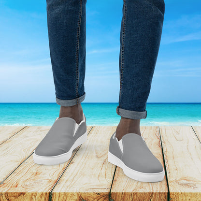 Gray slip-on shoes worn with blue jeans on a wooden platform with a beach background