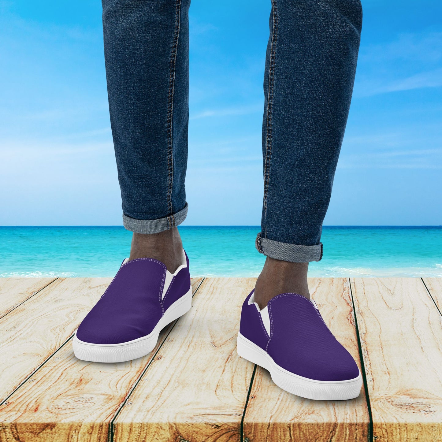Purple slip-on shoes worn with blue jeans against a beach background