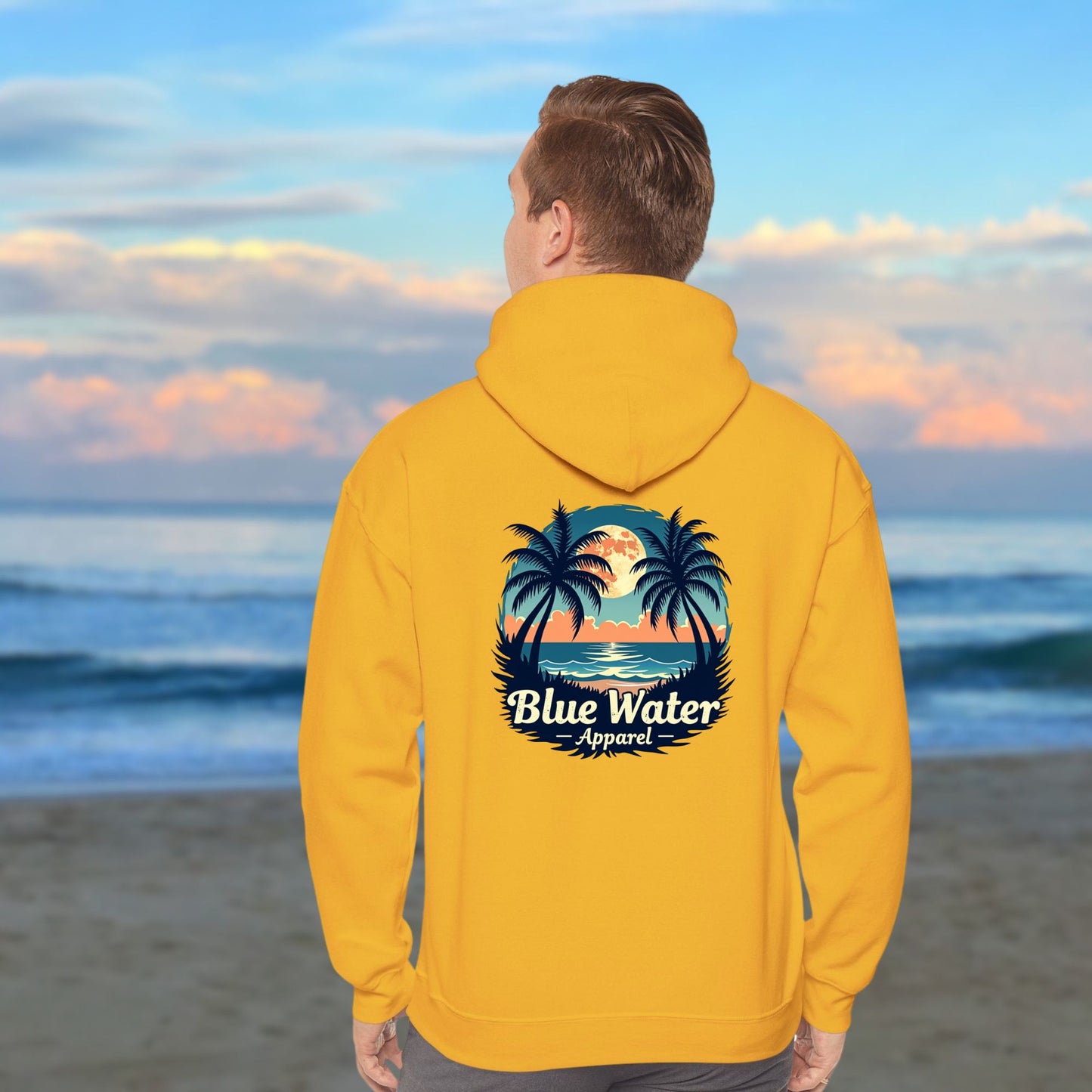 man on beach wearing gold tropical moon hoodie by blue water apparel