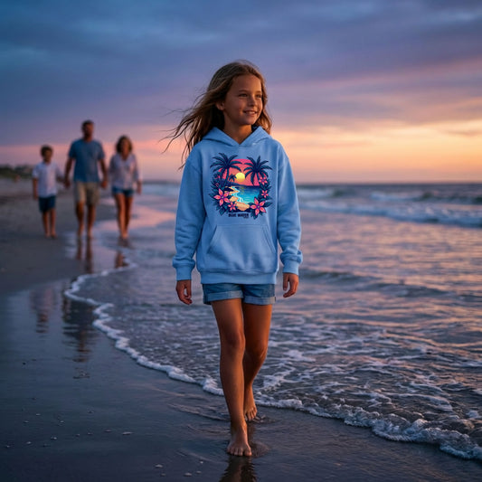 child model wearing carolina blue tropical sunset kids hoodie walking on beach with family in background by blue water apparel