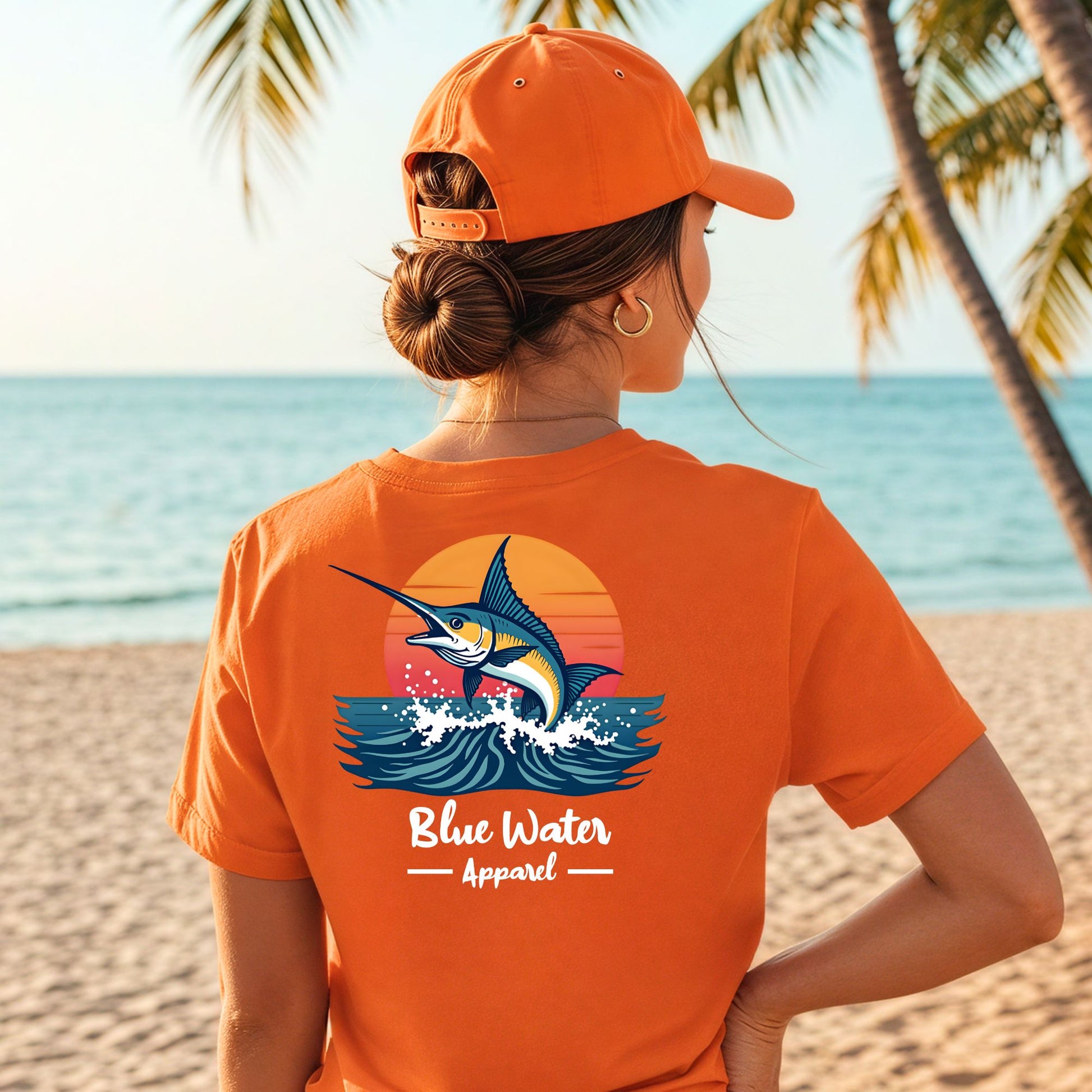 Model wearing an orange vintage marlin tee with the graphic on back on beach. 