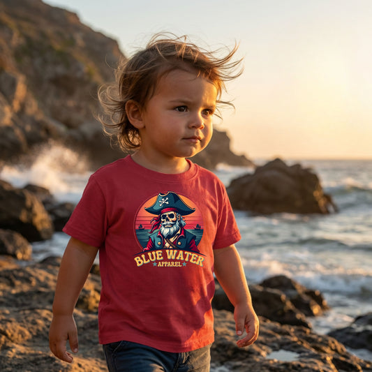 little boy wearing cardinal red vintage pirate kids tee walking on jetties of beach by blue water apparel