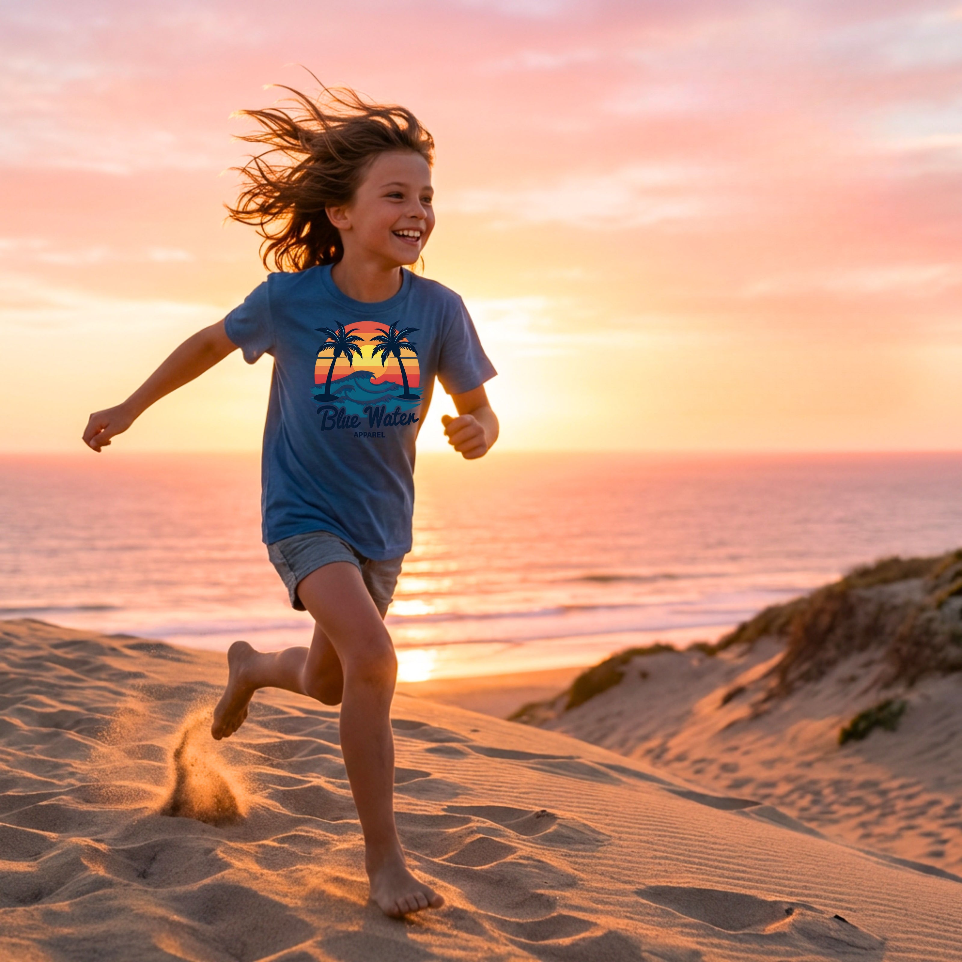 kid wearing indigo blue vintage sunset kid tee running across beach dune by blue water apparel