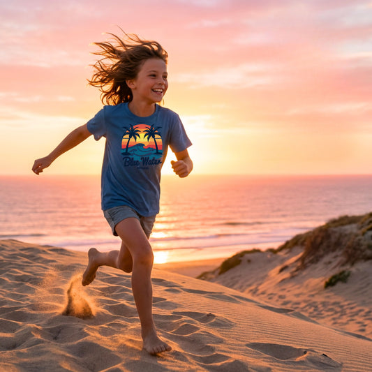 kid wearing indigo blue vintage sunset kid tee running across beach dune by blue water apparel