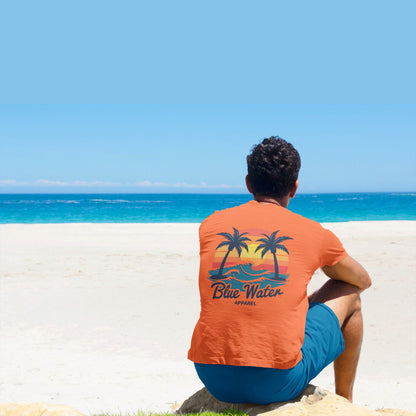 Model sitting on beach wearing orange Vintage Sunset tee by Blue Water Apparel