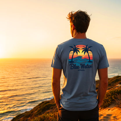 man wearing steel blue vintage sunset tee standing on seaside cliff by blue water apparel