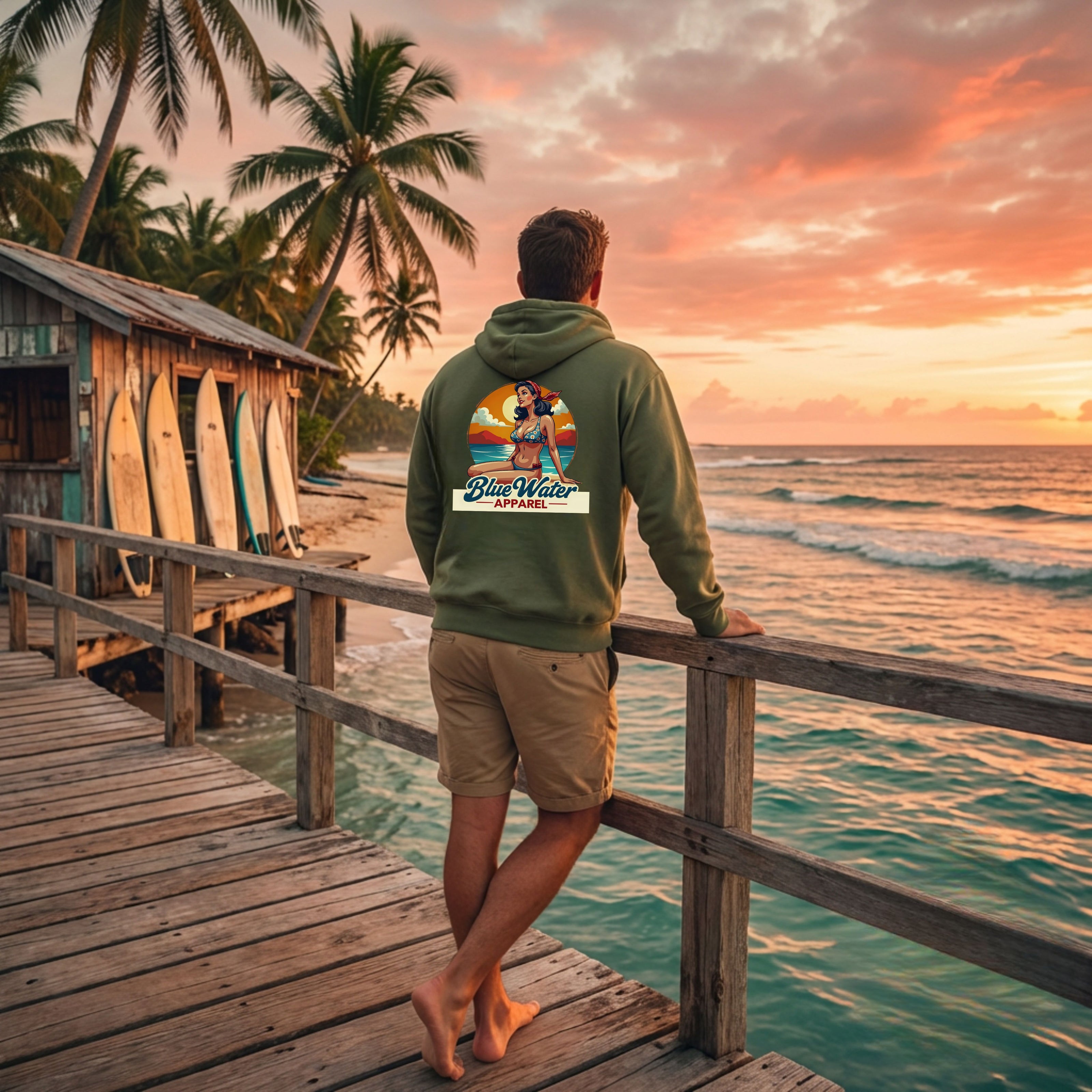 man wearing military green vintage pin-up hoodie on deck of surf shack by blue water apparel