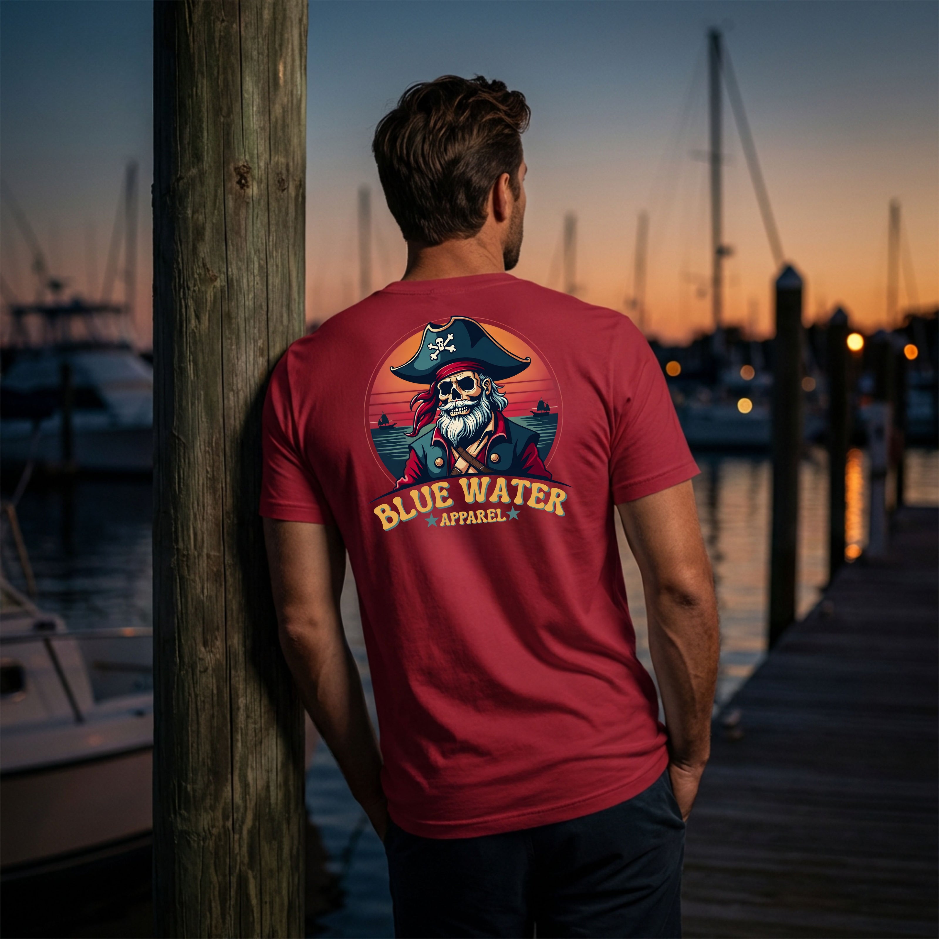 man wearing cardinal vintage pirate tee standing on dock at sunset by blue water apparel