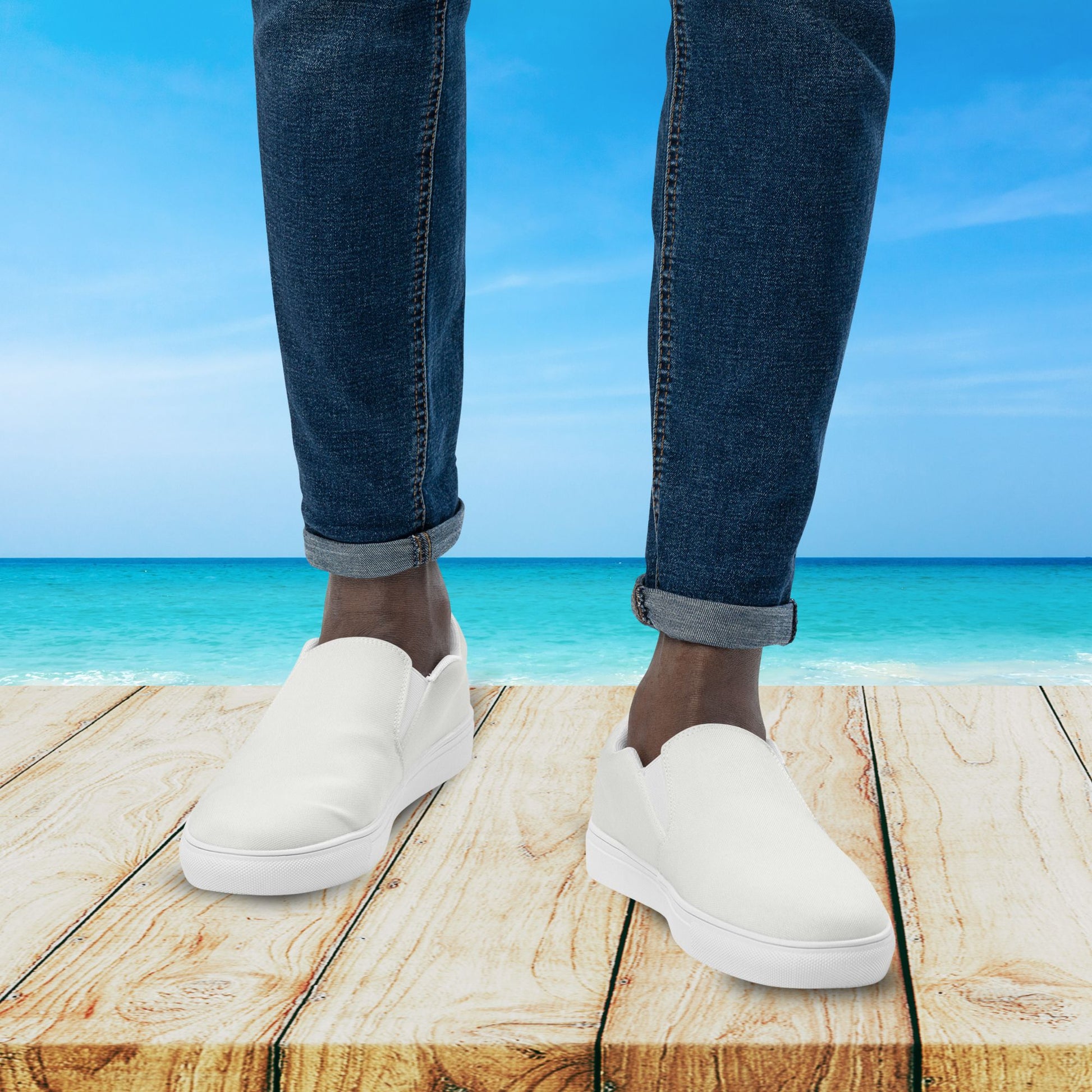 White sneakers worn on a wooden platform with a beach and blue sky in the background