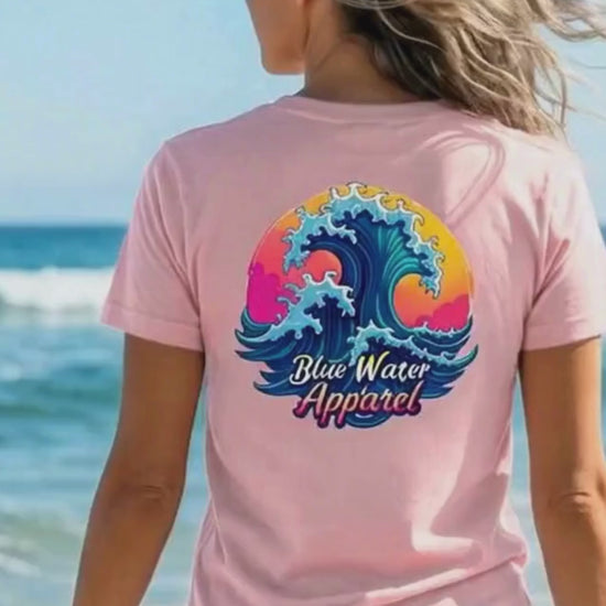 video of woman wearing pink retro wave adult tee walking towards ocean by blue water apparel.