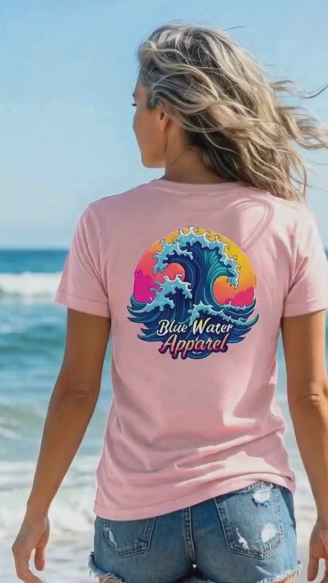 video of woman wearing pink retro wave adult tee walking towards ocean by blue water apparel.